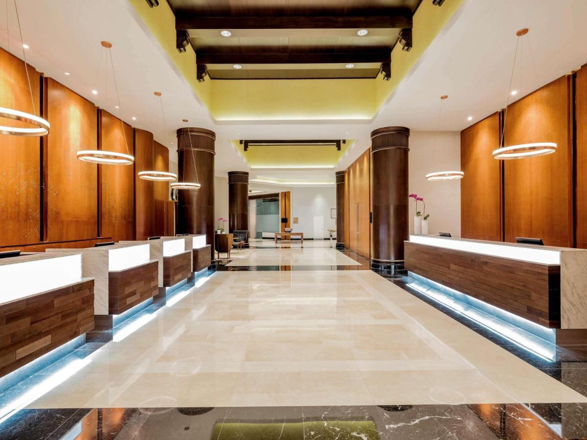 Paradox Singapore Merchant Court At Clarke Quay Exterior photo The photo shows a spacious and modern hotel lobby. It features several reception desks arranged along one side, each with a sleek, illuminated design. The walls are finished in warm wooden tones, and there are pendant lights hanging from the ceiling,