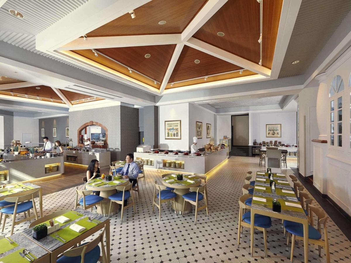 Paradox Singapore Merchant Court At Clarke Quay Exterior photo The photo depicts a modern restaurant interior. The space features a stylish design with a high ceiling and wooden details, creating an inviting atmosphere. 

Tables are neatly arranged, each set with green placemats and blue chairs. There is a secti