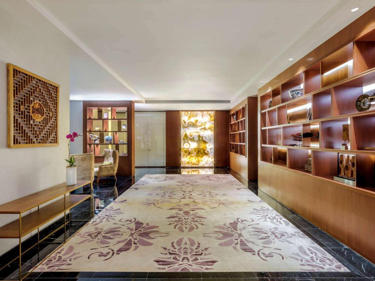 Paradox Singapore Merchant Court At Clarke Quay Exterior photo The photo shows a sleek and modern interior space, likely a lobby or lounge area. The floor is adorned with a large, elegant rug featuring floral patterns in soft colors. On one side, there is a wooden shelf filled with decorative items and books, al