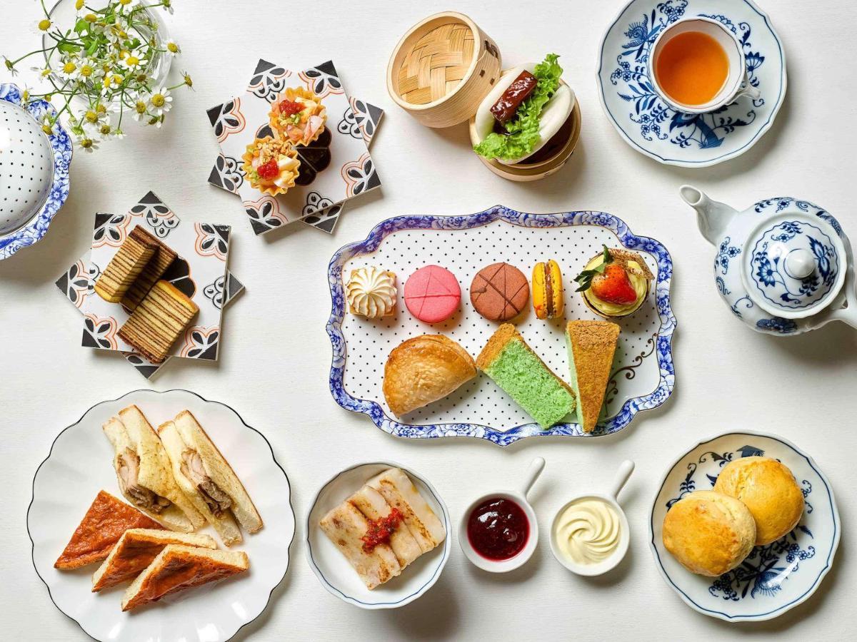 Paradox Singapore Merchant Court At Clarke Quay Exterior photo The photo displays a beautifully arranged assortment of food items, likely presented for an afternoon tea or dessert setting. 

- In the center, there is a decorative platter featuring a variety of pastries, including colorful macarons, small cakes, 