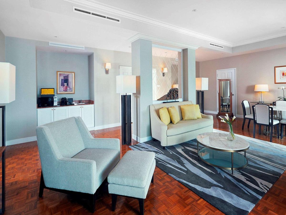 Paradox Singapore Merchant Court At Clarke Quay Exterior photo The photo shows a modern living space, which includes a seating area with a light-colored sofa that has yellow cushions, and an armchair with an ottoman. A round glass coffee table sits in the center on a patterned rug. In the background, there is a 