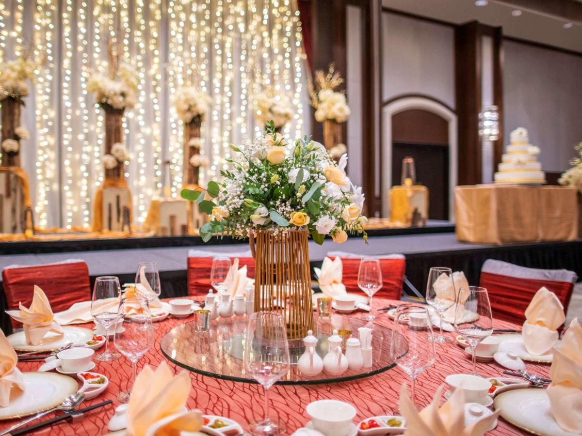 Paradox Singapore Merchant Court At Clarke Quay Exterior photo The photo depicts an elegantly arranged dining setup for a formal event. In the foreground, there is a round table covered with a textured red tablecloth. The table is adorned with various dining ware, including plates, cups, wine glasses, and beauti