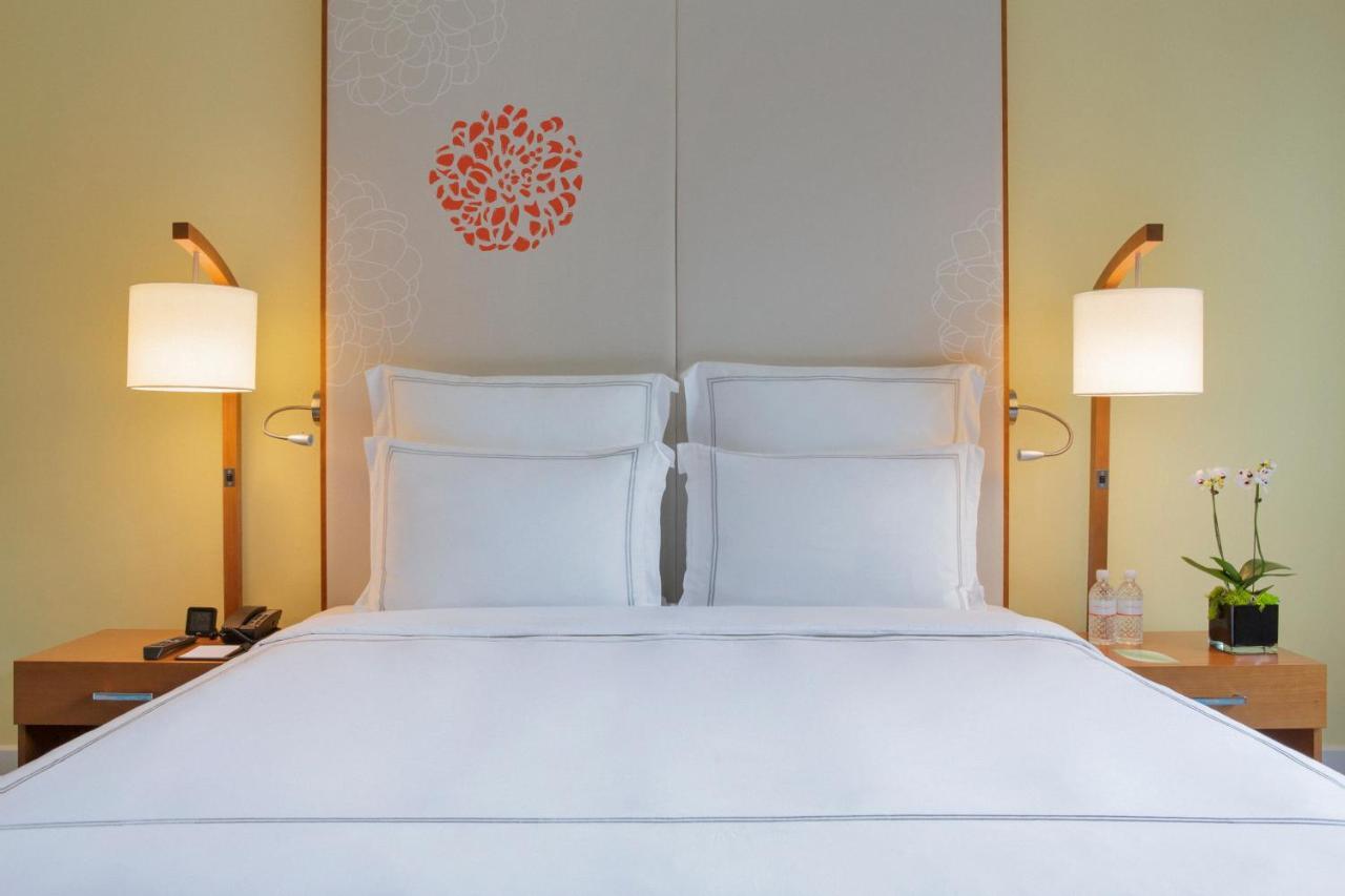 Paradox Singapore Merchant Court At Clarke Quay Exterior photo The photo showcases a cozy hotel room with a neatly made bed featuring white linens and two pillows. Behind the bed is a decorative headboard with a simple floral design in orange. On either side of the bed, there are stylish bedside lamps providing 