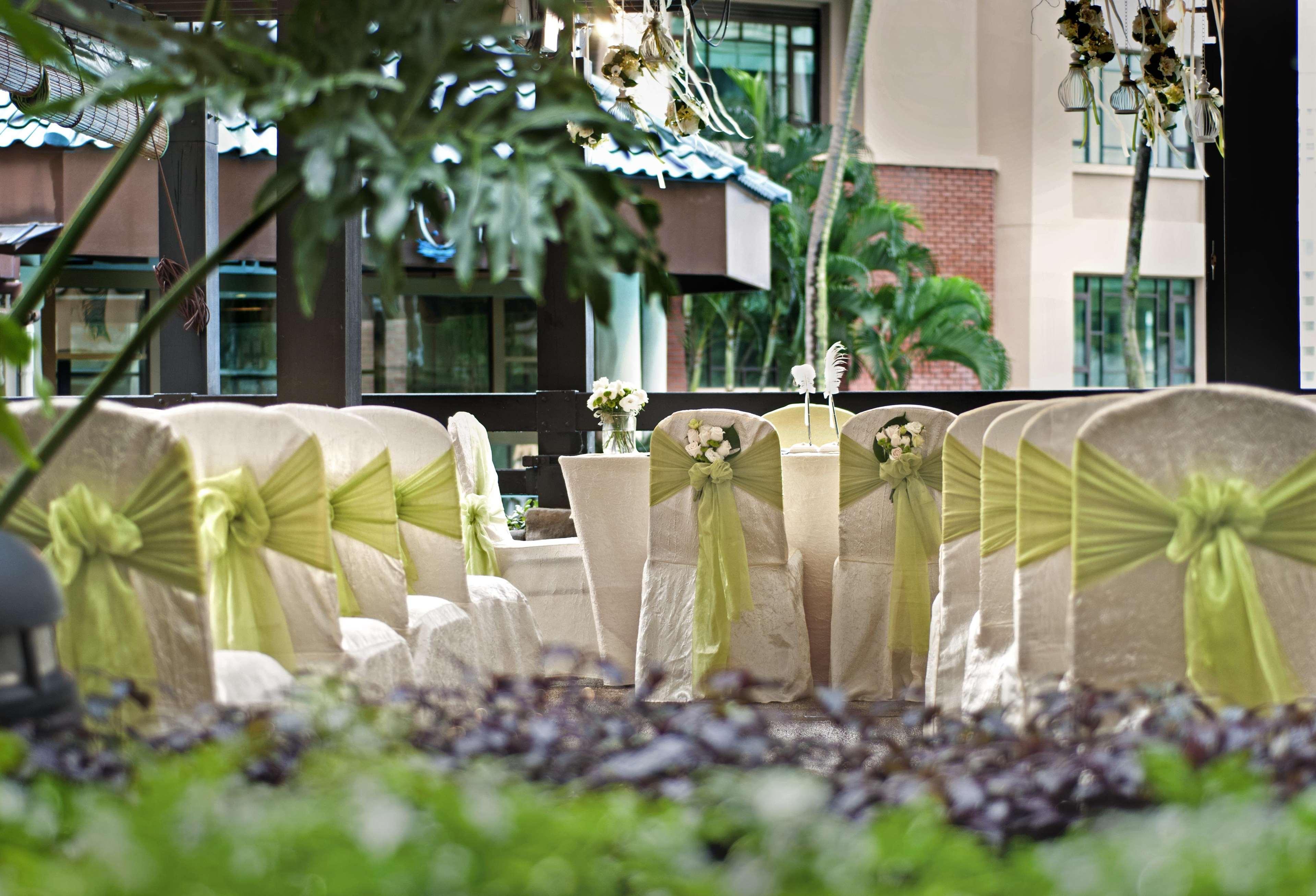 Paradox Singapore Merchant Court At Clarke Quay Exterior photo The photo shows a decorated setting for an event, likely a wedding or a formal gathering. There are several chairs covered in light fabric with green sashes tied around them, creating an elegant look. In the foreground, there are potted plants and gr