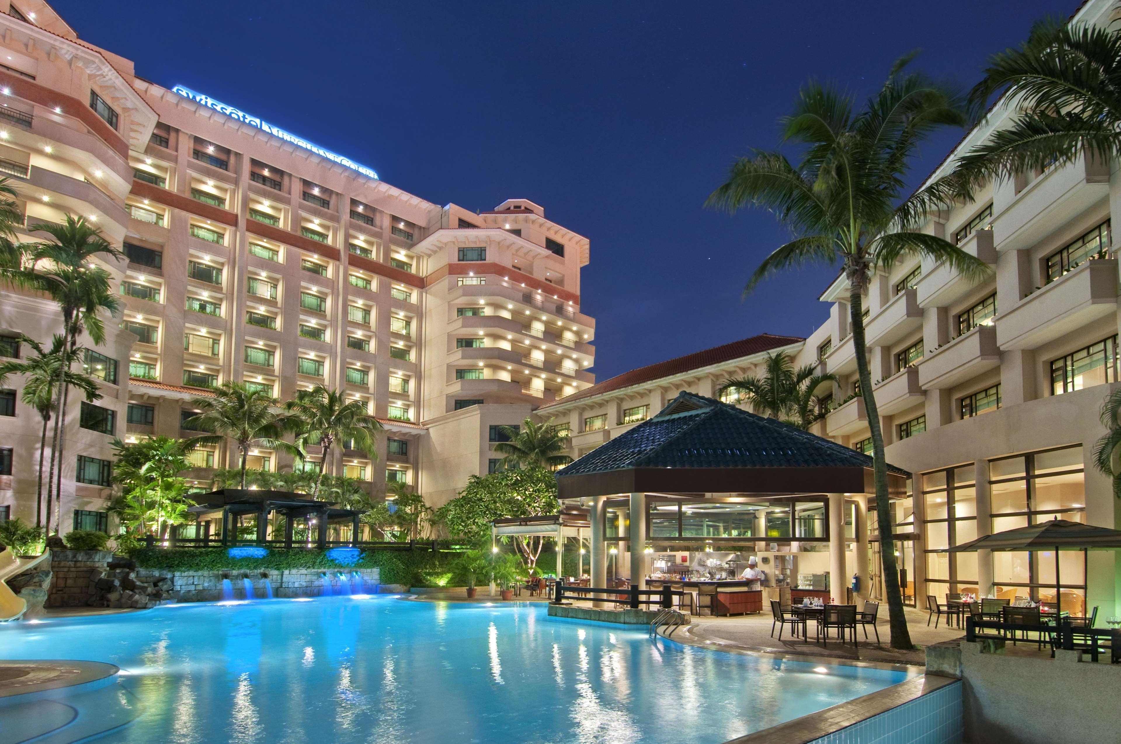 Paradox Singapore Merchant Court At Clarke Quay Facilities photo The photo depicts a modern hotel complex at night. The hotel buildings are illuminated, showcasing their architectural features. In the foreground, there is a large swimming pool, which reflects the lights from the surrounding area, creating a tranqu