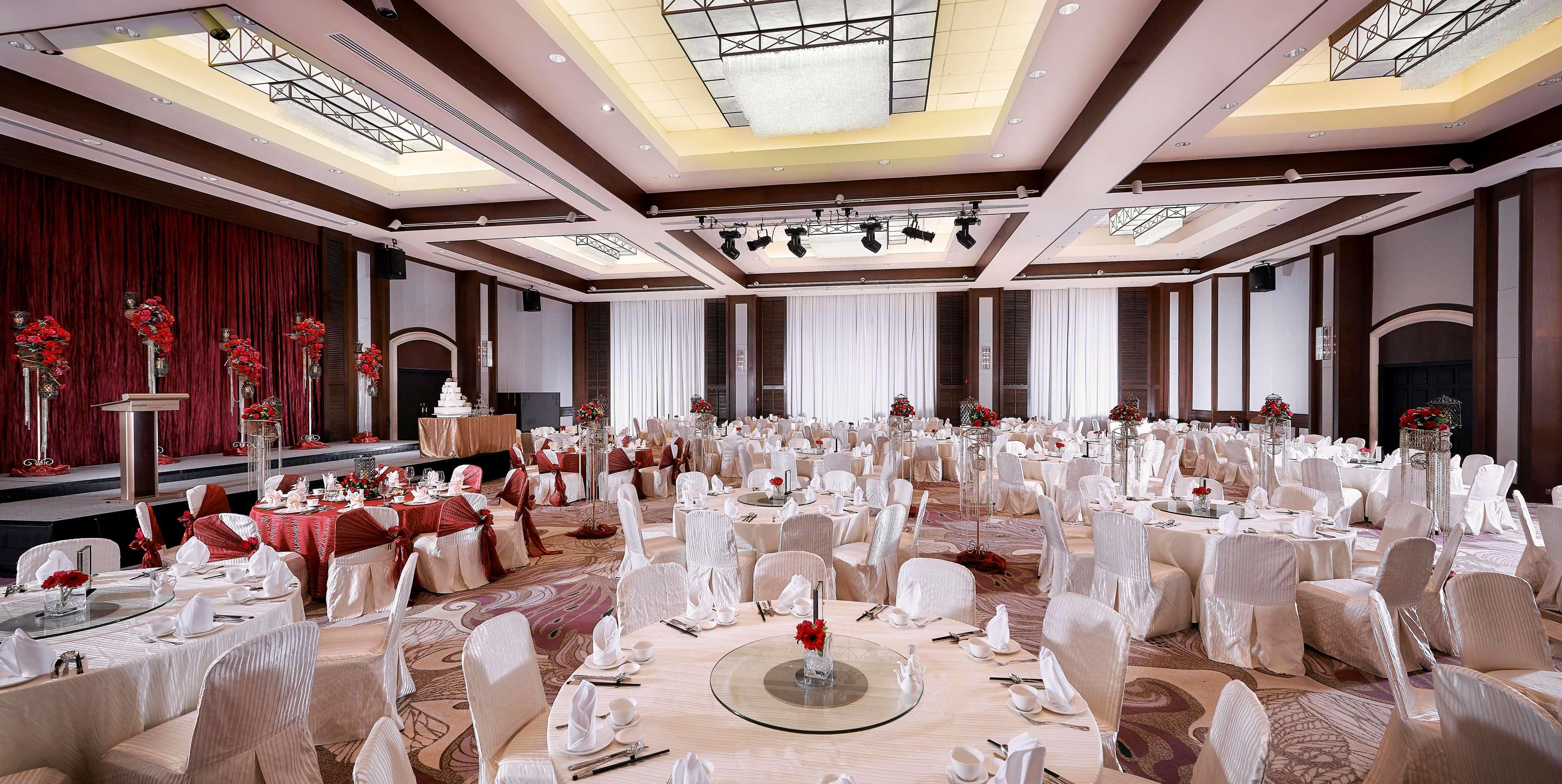 Paradox Singapore Merchant Court At Clarke Quay Exterior photo The photo shows a spacious banquet hall set up for an elegant event. Round tables are beautifully arranged, each covered with a tablecloth and adorned with a center decoration featuring red flowers. The chairs are draped in white covers, adding to th
