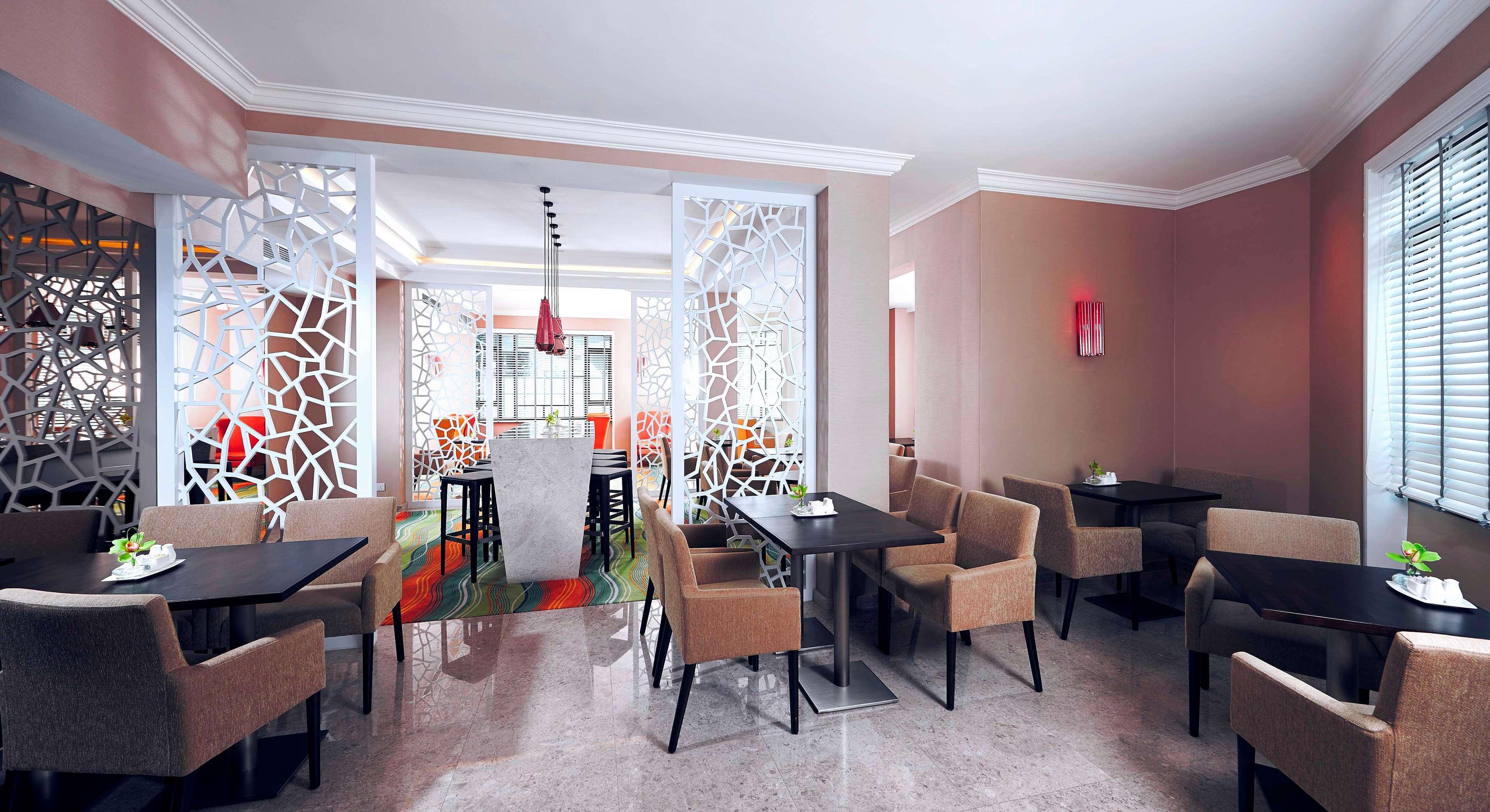 Paradox Singapore Merchant Court At Clarke Quay Exterior photo The image shows an interior view of a modern restaurant or café. It features a well-decorated space with light-colored walls and a polished floor. The dining area has several tables with dark wooden surfaces, surrounded by beige upholstered chairs. 
