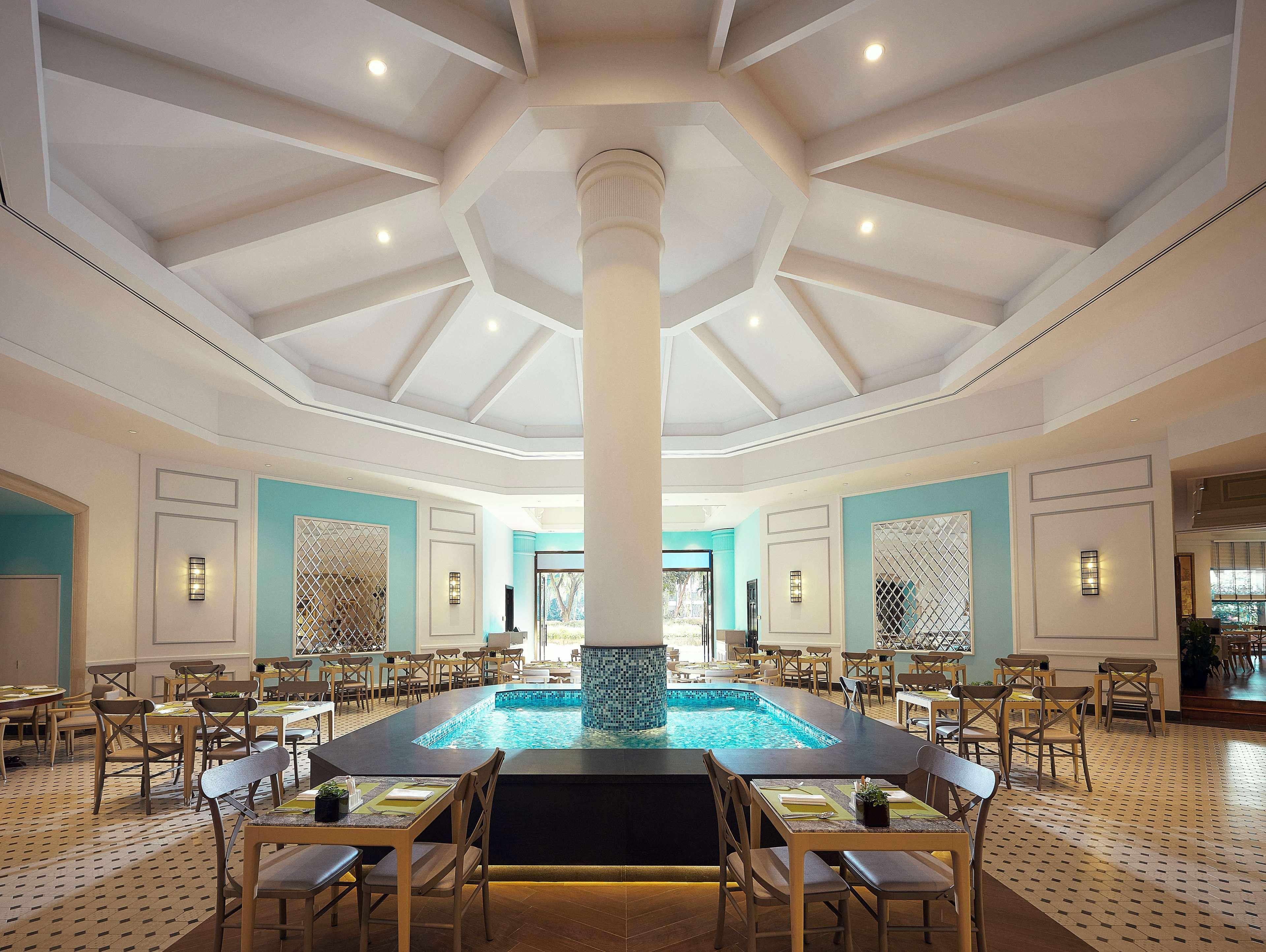 Paradox Singapore Merchant Court At Clarke Quay Exterior photo The photo shows an elegant dining area with a spacious, open layout. There is a large column in the center, surrounded by a circular water feature that adds a serene atmosphere. The ceiling is designed with a geometric pattern, giving it a modern loo