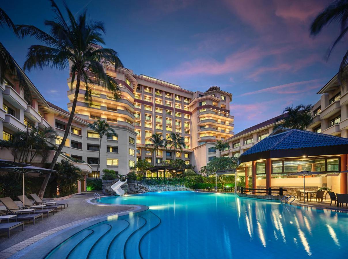 Paradox Singapore Merchant Court At Clarke Quay Exterior photo The photo shows a luxurious hotel building, featuring multiple stories and a modern architectural design. In front of the hotel, there is a large, inviting swimming pool that is illuminated in a vibrant blue hue, suggesting it may be an evening setti
