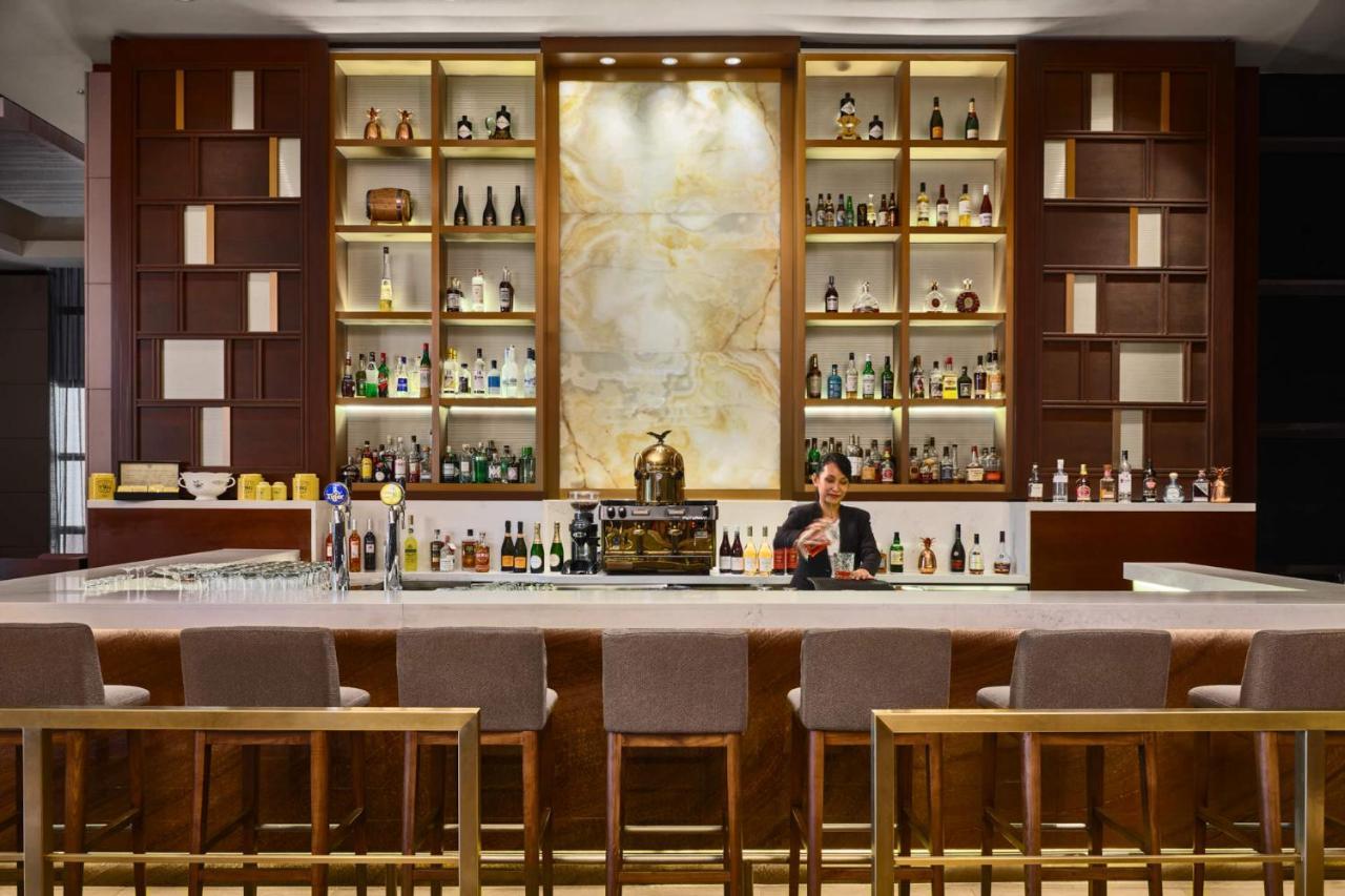 Paradox Singapore Merchant Court At Clarke Quay Exterior photo The photo shows a well-designed bar area. The bar has a long counter with high stools arranged in front. Behind the bar, there is an elegant display of various bottles of spirits, arranged on shelves with a stylish backdrop. The shelves feature a com