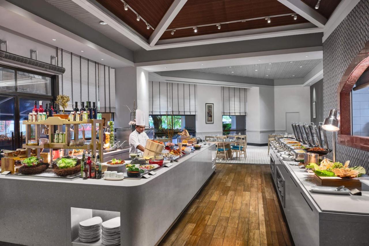 Paradox Singapore Merchant Court At Clarke Quay Exterior photo The photo depicts a modern buffet restaurant setting. There is a spacious area with a well-organized serving station along the counter, featuring a variety of food options, including fresh salads and other dishes. A chef in a white uniform is engaged