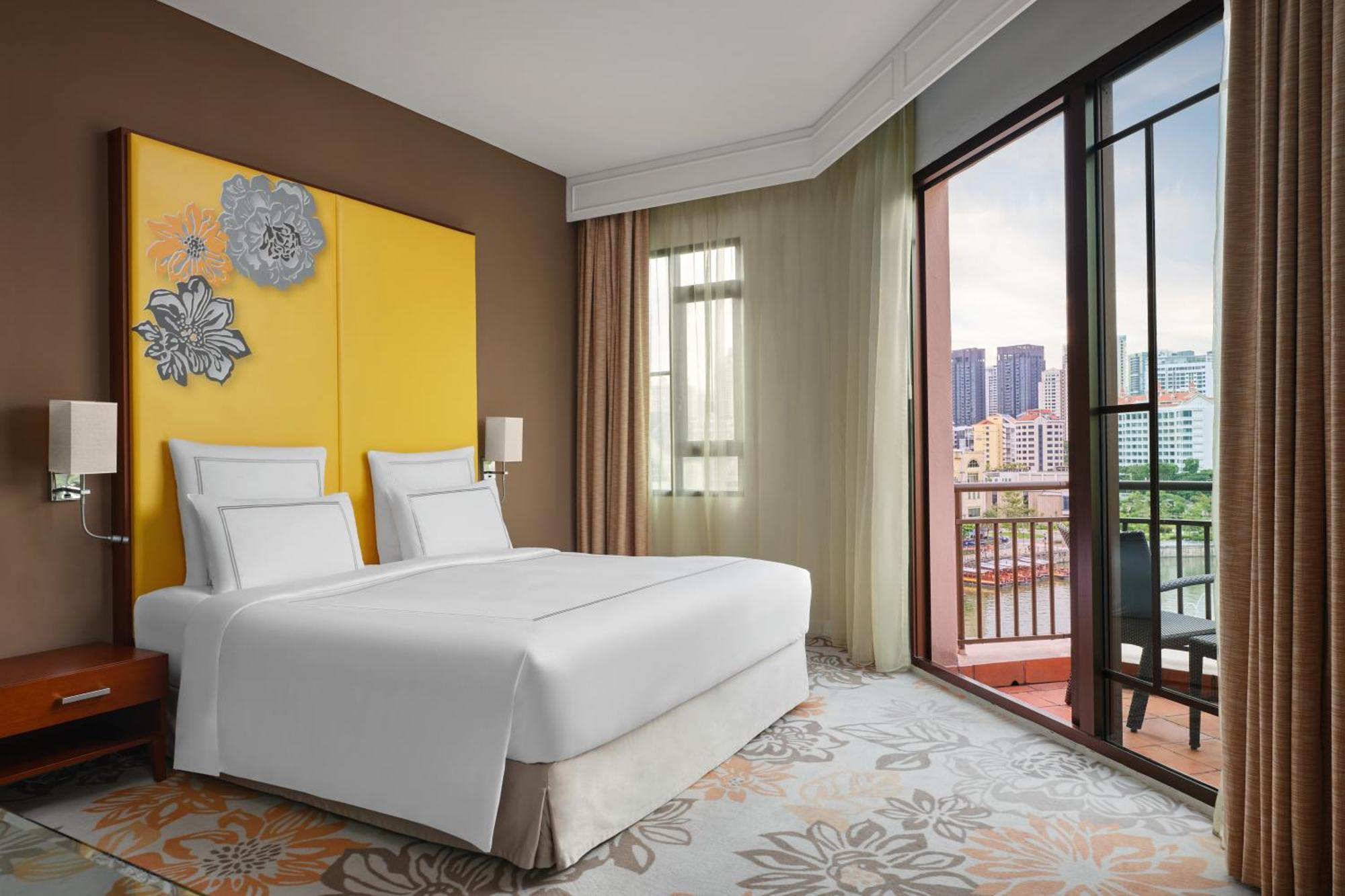 Paradox Singapore Merchant Court At Clarke Quay Exterior photo The photo shows a modern hotel room featuring two beds with white linens placed against a yellow accent wall adorned with decorative elements. The room has large windows with sheer curtains, allowing natural light to enter and offering a view of the 