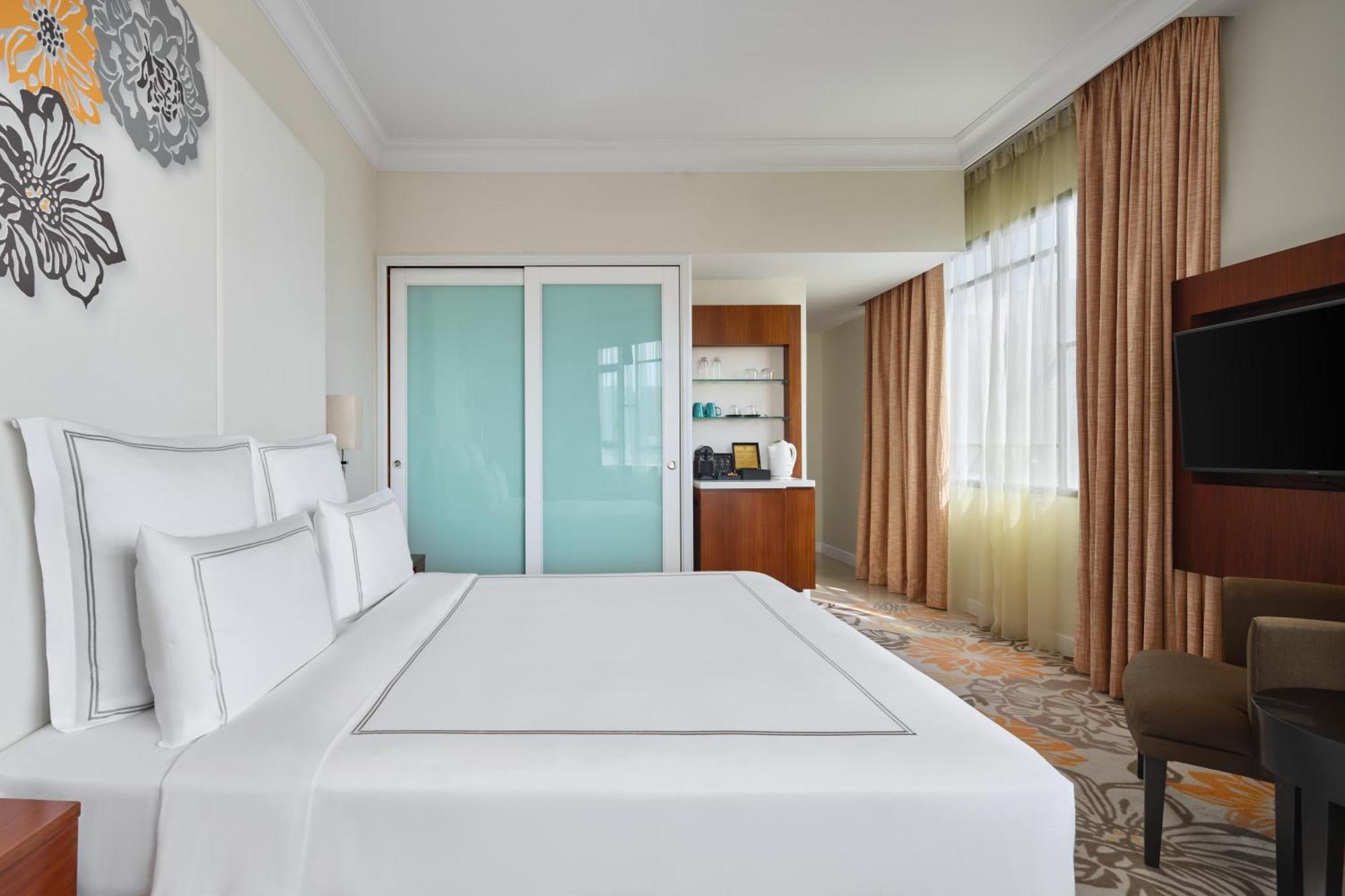 Paradox Singapore Merchant Court At Clarke Quay Exterior photo The photo shows a well-decorated hotel room featuring a large bed with crisp white linens. There are several white pillows arranged neatly on the bed. To the side, there are glass sliding doors leading to another area, which appears to be a closet or